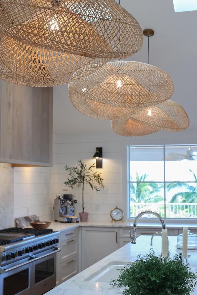 kitchen featuring light stone counters, double oven range, a sink, pendant lighting, and backsplash