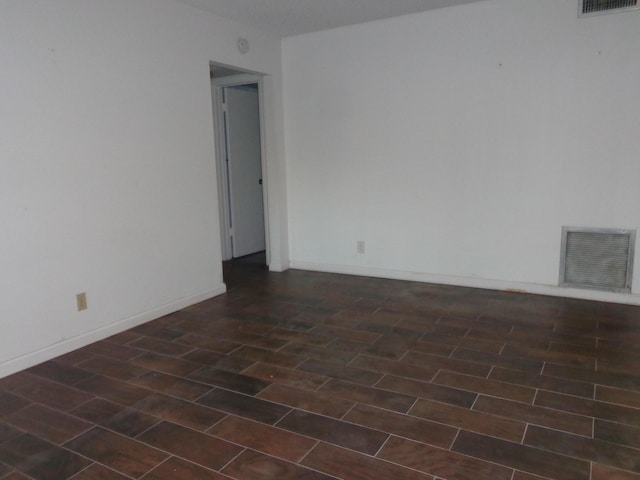 unfurnished room featuring visible vents, baseboards, and dark wood finished floors