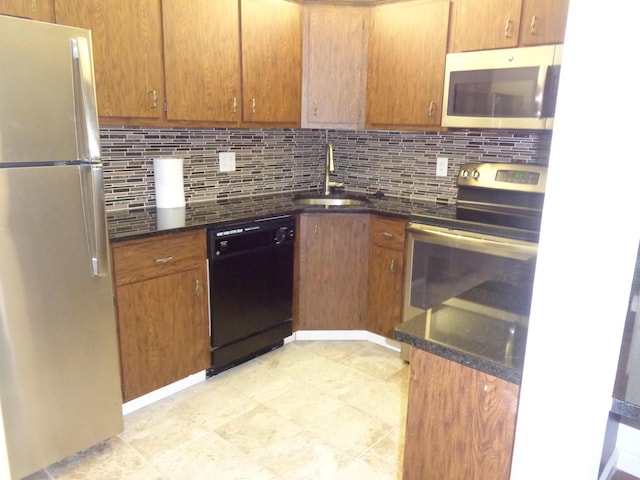 kitchen featuring a sink, dark stone counters, appliances with stainless steel finishes, brown cabinetry, and decorative backsplash