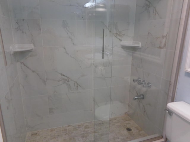 bathroom featuring a marble finish shower and toilet