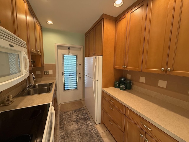 kitchen featuring tasteful backsplash, light tile patterned floors, brown cabinetry, white appliances, and a sink