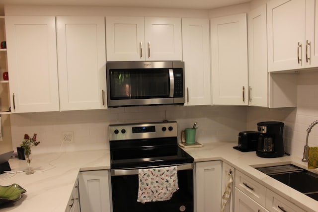 kitchen featuring white cabinets, light stone countertops, stainless steel appliances, and a sink