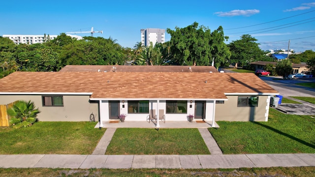 ranch-style home featuring a front lawn, roof with shingles, and stucco siding