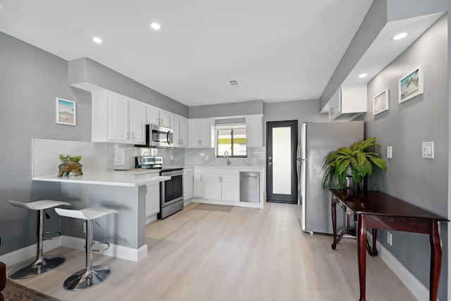 kitchen with visible vents, backsplash, a peninsula, white cabinets, and stainless steel appliances