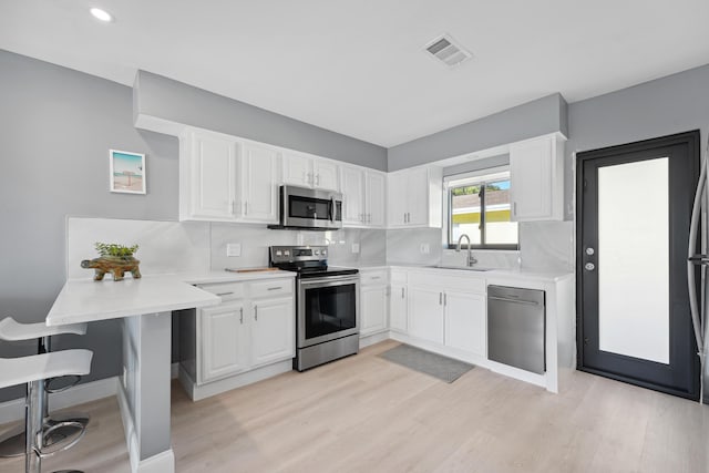 kitchen with a peninsula, a sink, light countertops, white cabinets, and appliances with stainless steel finishes