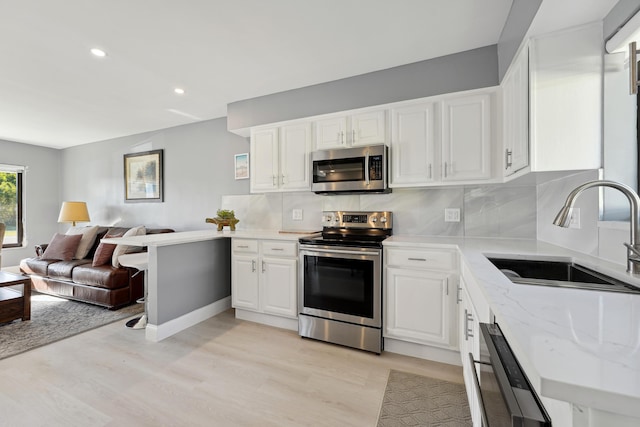 kitchen with a sink, open floor plan, white cabinetry, stainless steel appliances, and light wood-style floors