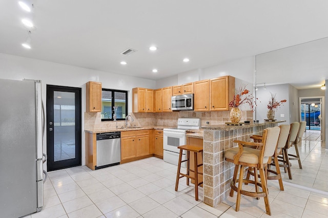 kitchen featuring a peninsula, a sink, stainless steel appliances, a kitchen breakfast bar, and backsplash