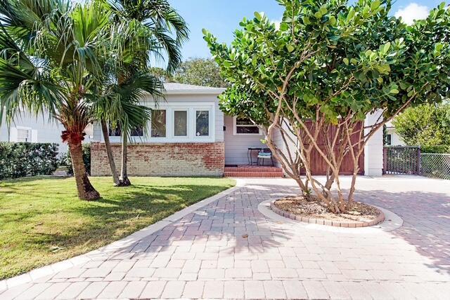 view of front facade with brick siding, decorative driveway, a front lawn, and fence