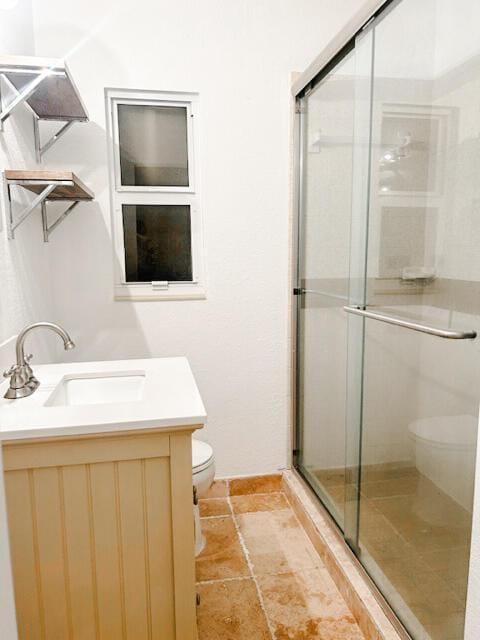 bathroom with stone tile floors, a shower stall, toilet, and vanity