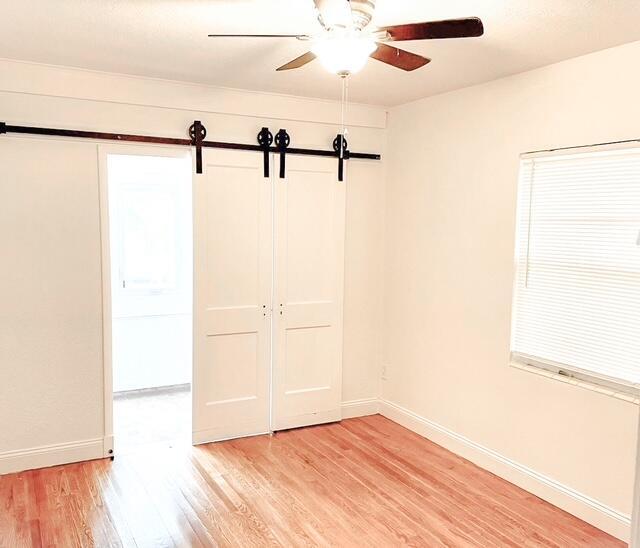 spare room with a barn door, baseboards, light wood finished floors, and ceiling fan