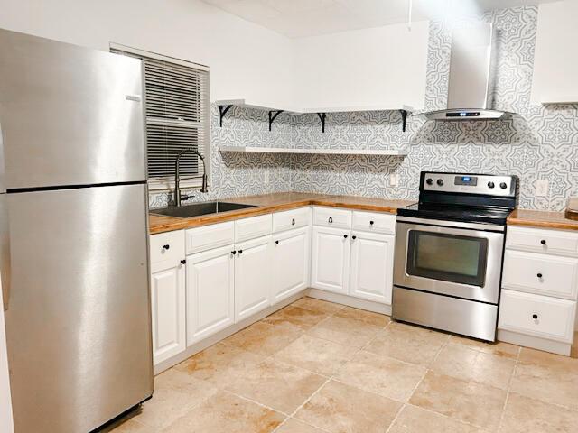 kitchen featuring wood counters, stainless steel appliances, white cabinetry, wall chimney exhaust hood, and a sink