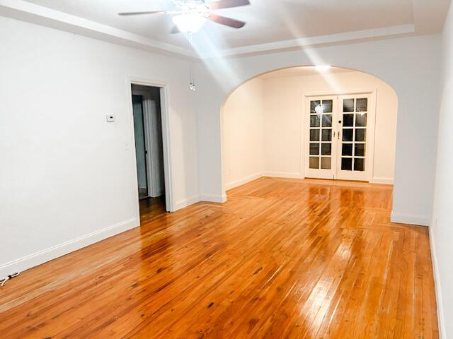 empty room featuring baseboards, arched walkways, light wood-style flooring, and a ceiling fan