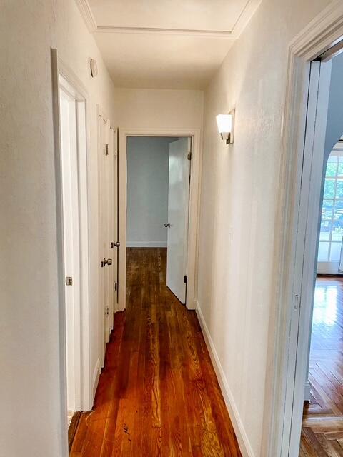 corridor featuring arched walkways, baseboards, and wood finished floors