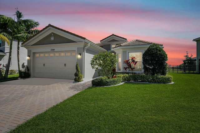 view of front of house featuring stucco siding, a tile roof, decorative driveway, a yard, and a garage