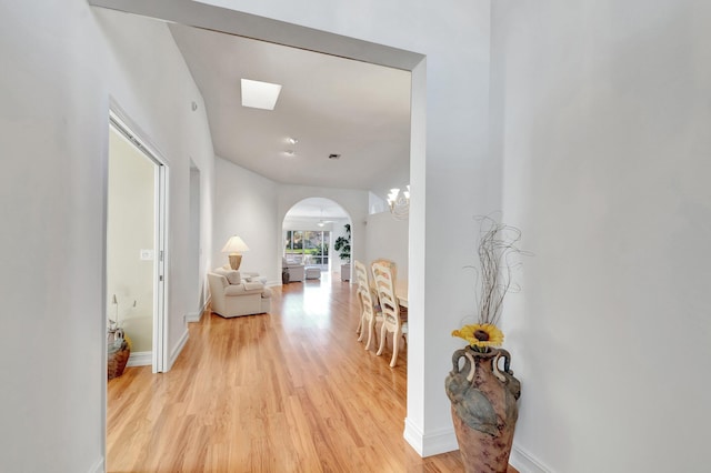 hallway featuring arched walkways, baseboards, and light wood-style floors