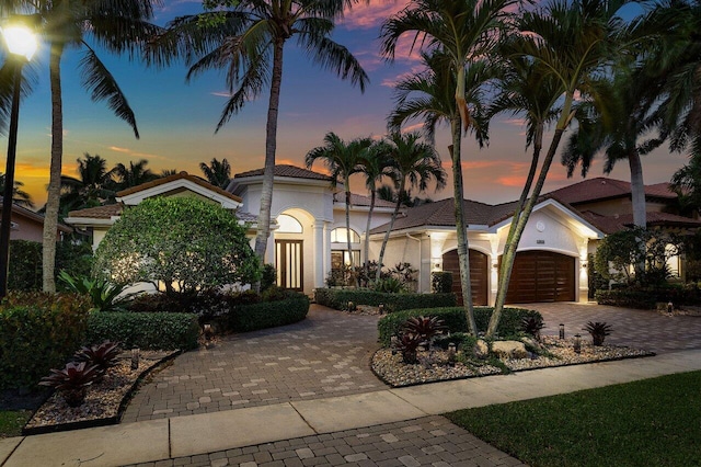 mediterranean / spanish house with stucco siding, an attached garage, a tile roof, and decorative driveway