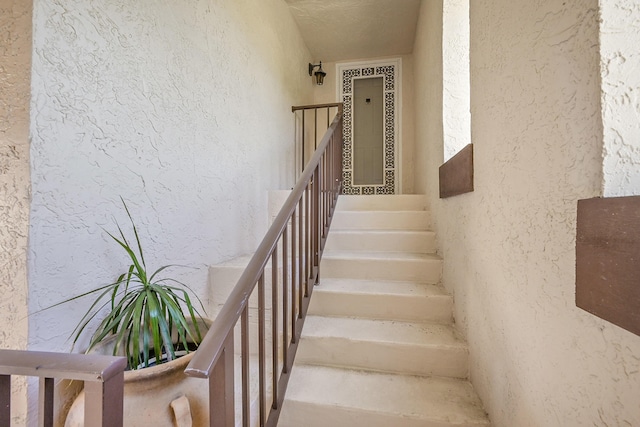 stairs with a textured ceiling and a textured wall