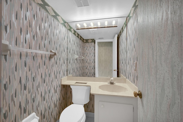 bathroom with visible vents, toilet, vanity, and wallpapered walls