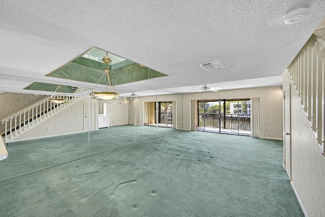 unfurnished living room with visible vents, wooden walls, carpet flooring, and stairway