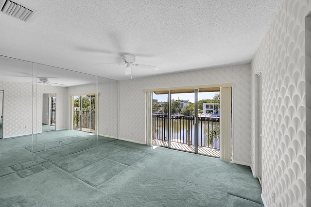 carpeted empty room with visible vents, a water view, a textured ceiling, wallpapered walls, and ceiling fan