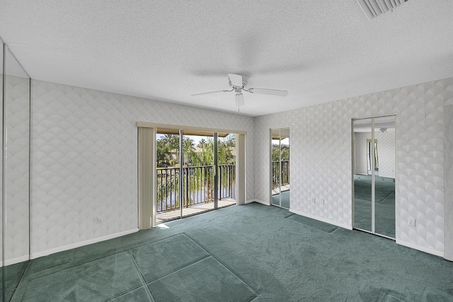 carpeted empty room with wallpapered walls, baseboards, visible vents, and a textured ceiling