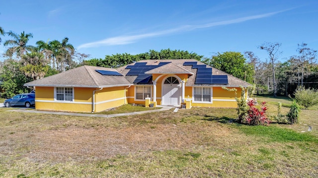 view of front facade featuring stucco siding, roof mounted solar panels, and a front lawn