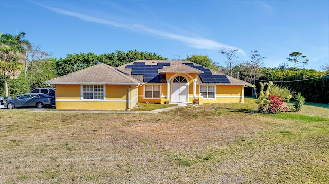 single story home featuring stucco siding, solar panels, a front yard, and a shingled roof