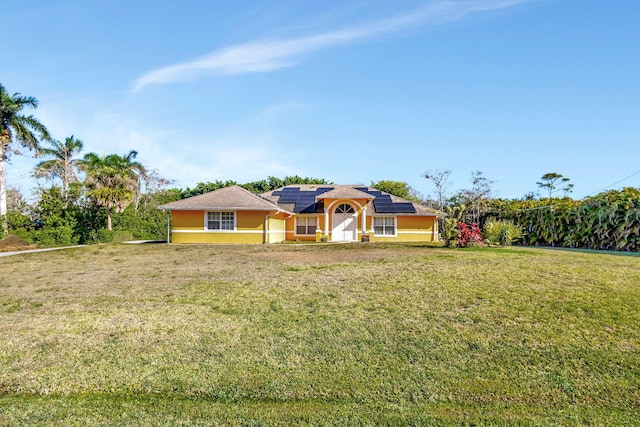 ranch-style home with roof mounted solar panels, stucco siding, and a front lawn