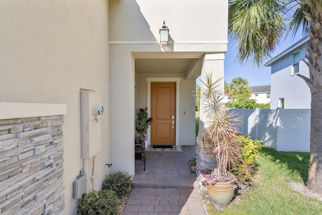 doorway to property featuring stucco siding and fence