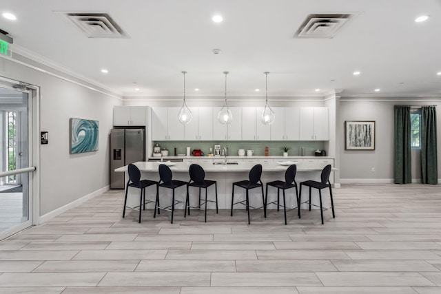 kitchen featuring visible vents, a sink, a large island, light countertops, and stainless steel refrigerator with ice dispenser