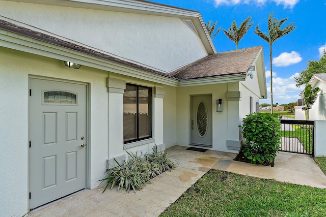 property entrance featuring stucco siding, a shingled roof, and fence