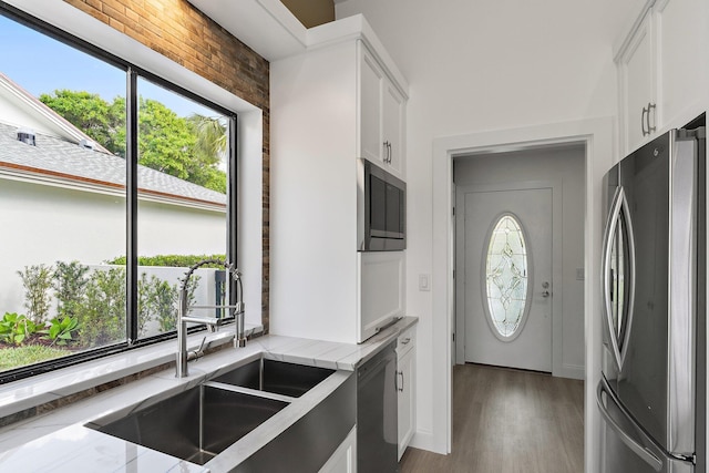 kitchen with light stone countertops, light wood-style flooring, a sink, stainless steel appliances, and white cabinets