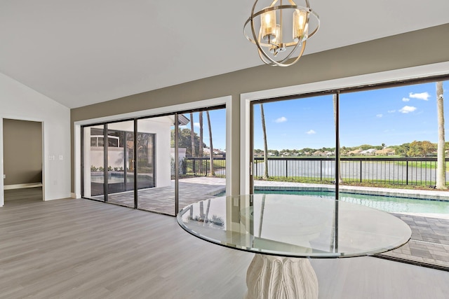 interior space with baseboards, a water view, lofted ceiling, an inviting chandelier, and wood finished floors