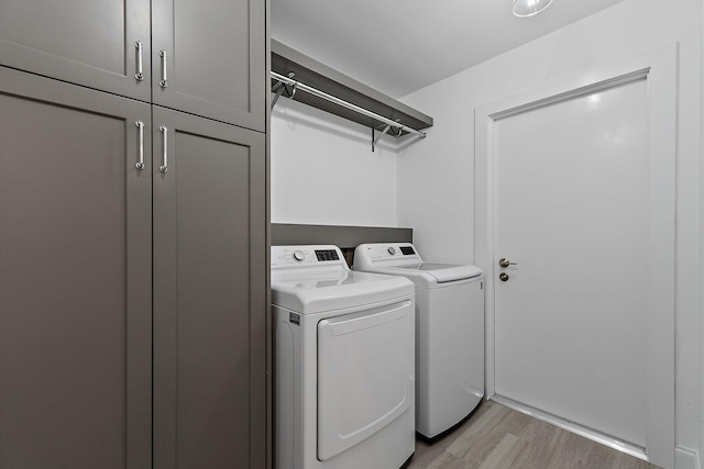 laundry area with washer and clothes dryer, cabinet space, and light wood finished floors