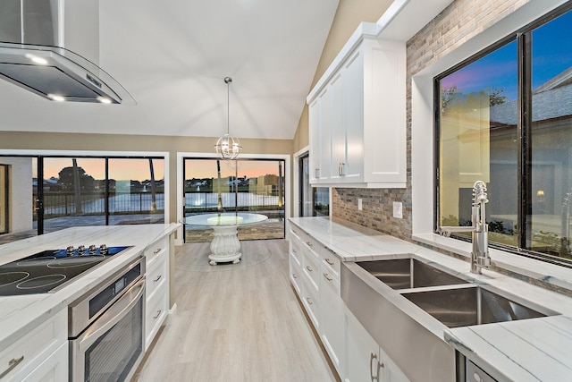 kitchen featuring oven, black electric stovetop, wall chimney exhaust hood, and light stone countertops