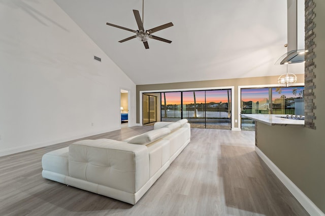 unfurnished living room featuring wood finished floors, visible vents, baseboards, high vaulted ceiling, and a water view