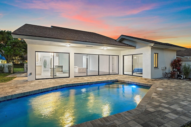 back of house at dusk featuring stucco siding, an outdoor pool, a patio, and a gate