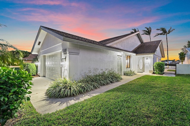 property exterior at dusk with a gate, fence, stucco siding, a garage, and a lawn