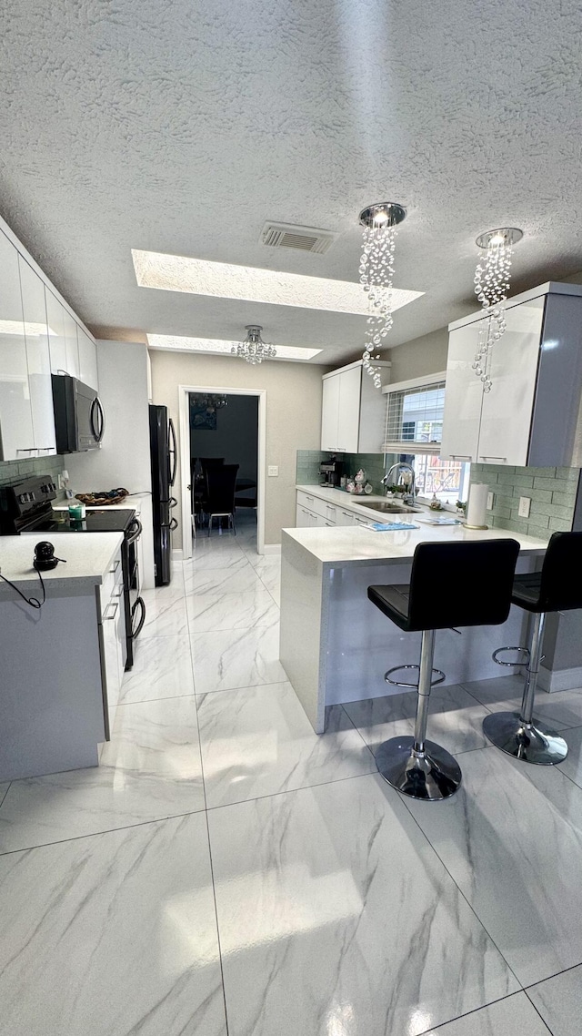 kitchen with visible vents, a peninsula, black appliances, white cabinetry, and marble finish floor