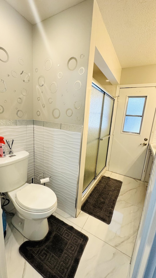 bathroom featuring a stall shower, a textured ceiling, tile walls, toilet, and marble finish floor