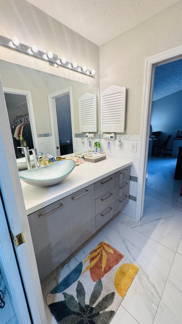 full bath with tile walls, double vanity, marble finish floor, a textured ceiling, and a sink