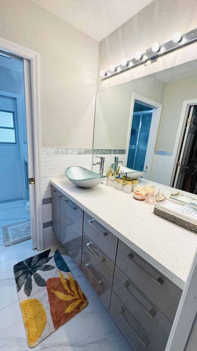 bathroom featuring a wainscoted wall, a textured ceiling, vanity, and a textured wall