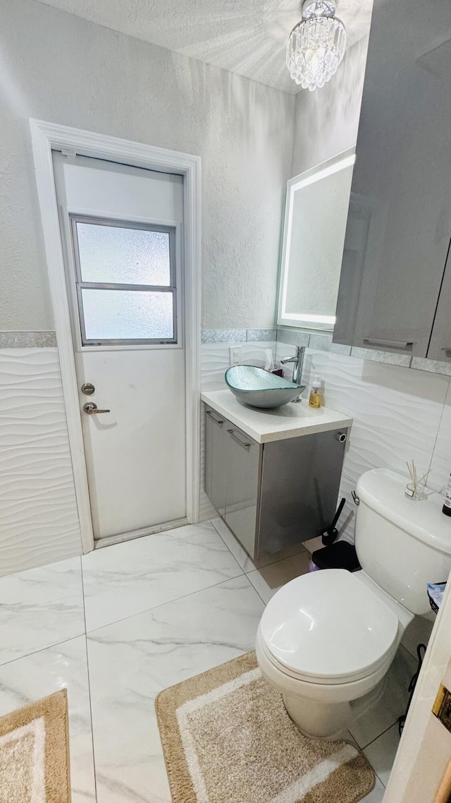 half bathroom featuring toilet, wainscoting, a textured wall, marble finish floor, and vanity