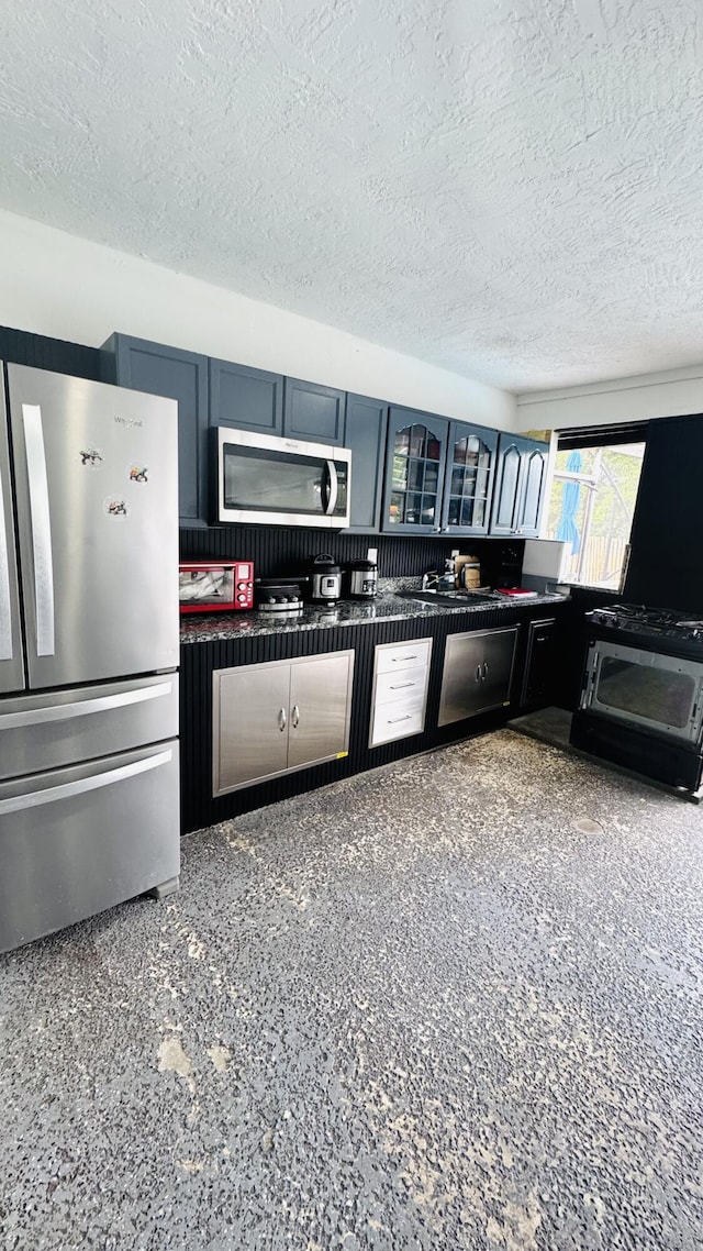 kitchen with a textured ceiling, dark countertops, glass insert cabinets, and stainless steel appliances