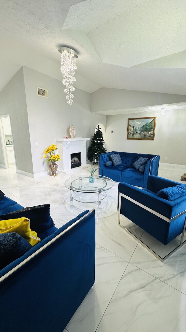 living area with visible vents, a fireplace with raised hearth, lofted ceiling, an inviting chandelier, and marble finish floor