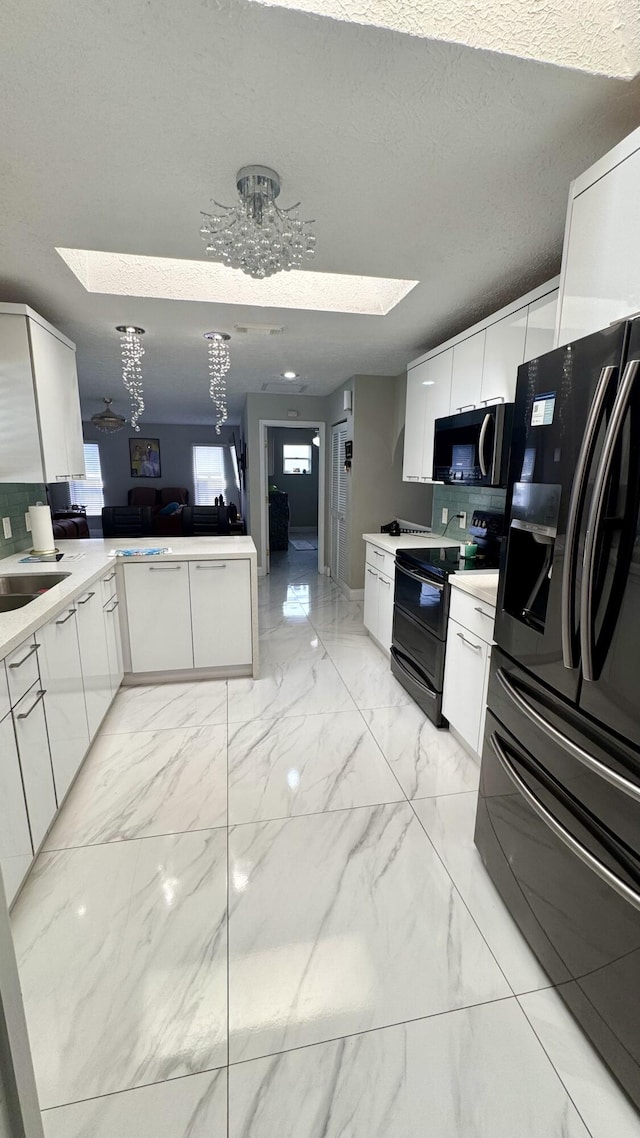 kitchen featuring a skylight, marble finish floor, white cabinets, and black appliances