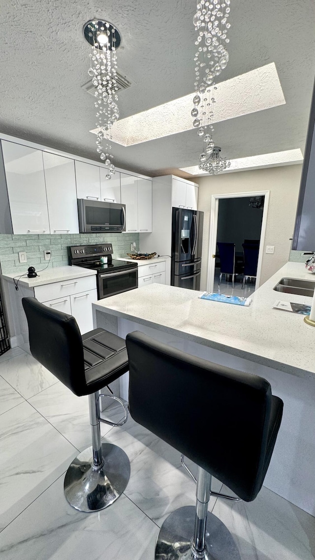 kitchen with a sink, stainless steel appliances, marble finish floor, white cabinetry, and tasteful backsplash