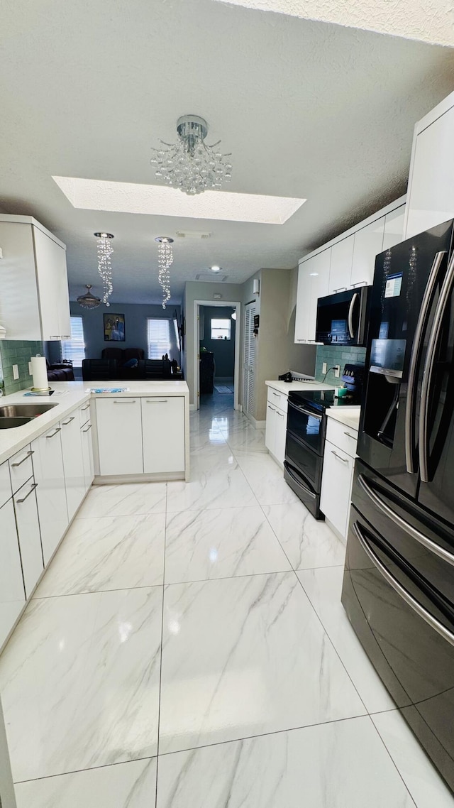 kitchen with a skylight, marble finish floor, black appliances, and a sink