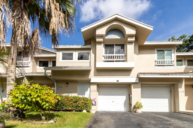 view of property with stucco siding, an attached garage, driveway, and a balcony