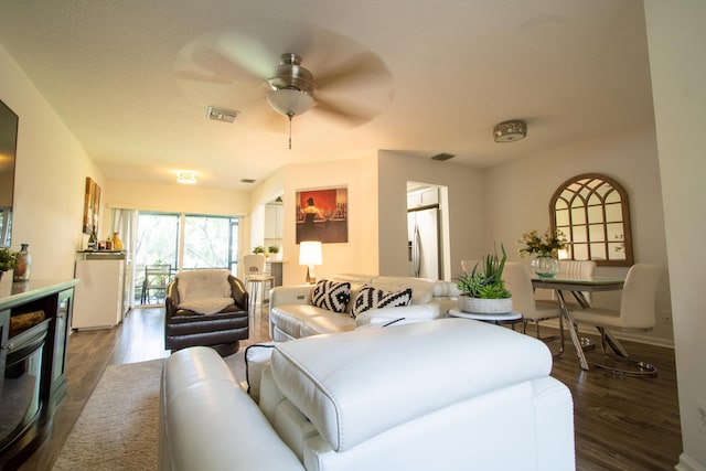 living area with visible vents, a ceiling fan, and dark wood-style flooring